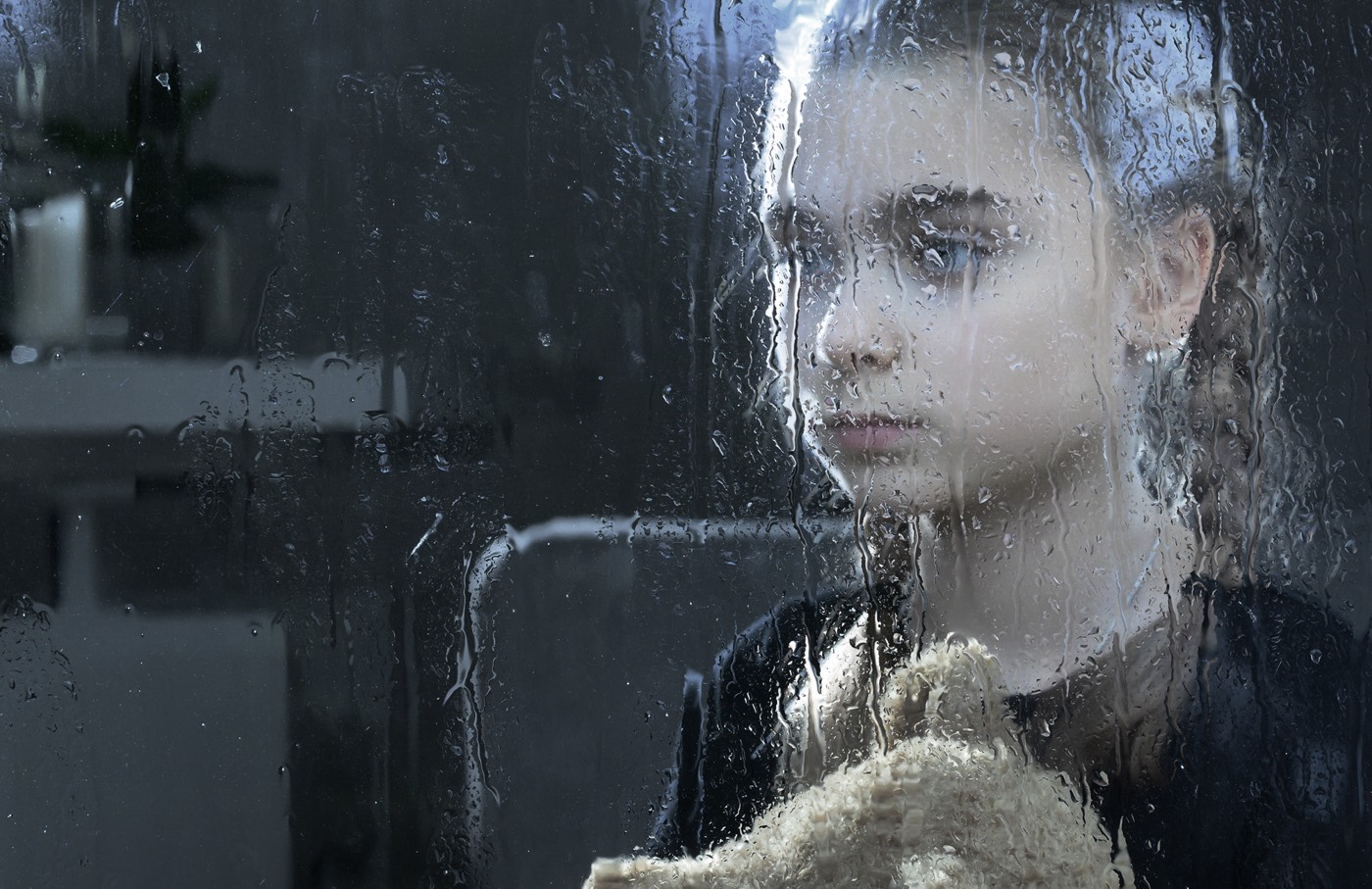 A young girl behind the rain-damp window, representing a symbol of deteriorating mental health