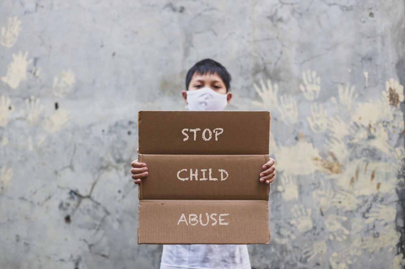 Young man with his mask displays a protest message: STOP CHILD ABUSE