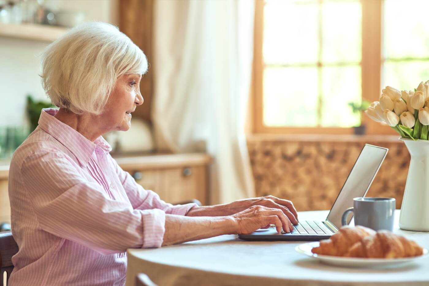 Elderly woman at home using her laptop to check her direct deposit