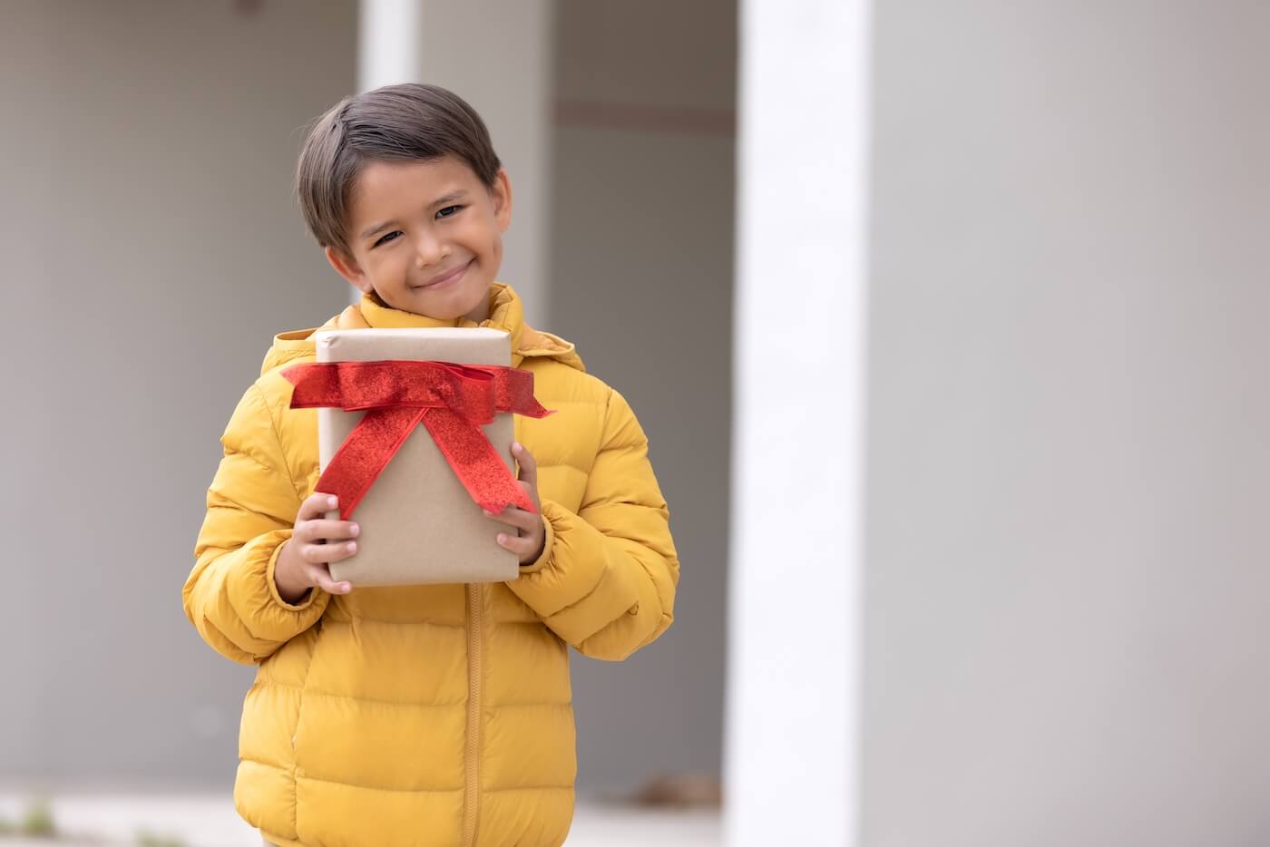 Un garçon en manteau d'hiver tenant un coffret de don et souriant.