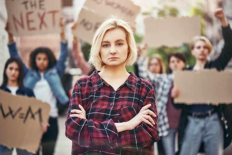 Une jeune femme blonde se tient debout les bras croisés lors d'une manifestation sur le droit des femmes