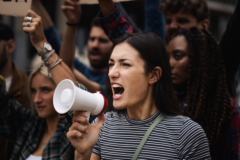 A young woman protester demonstrates shouting loudly through a megaphone on women's rights