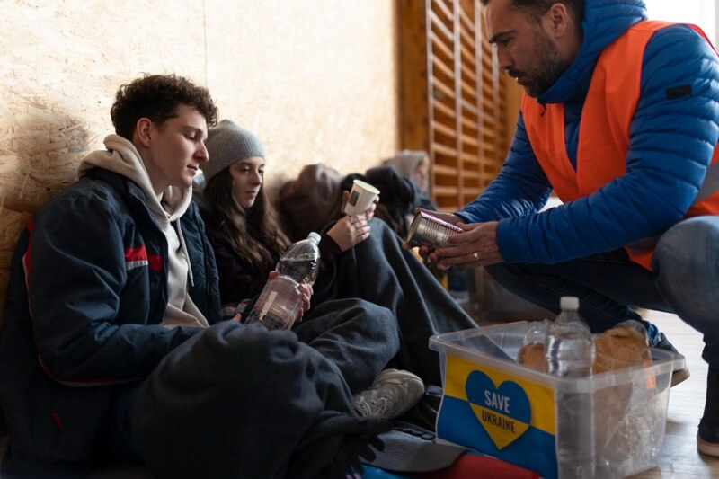 Ukrainian war refugees in a temporary shelter and aid center receive water from volunteers.