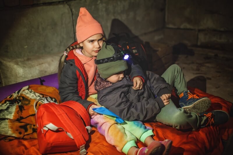 Children wearing winter coats with the Ukrainian flag, stand in an air-raid shelter