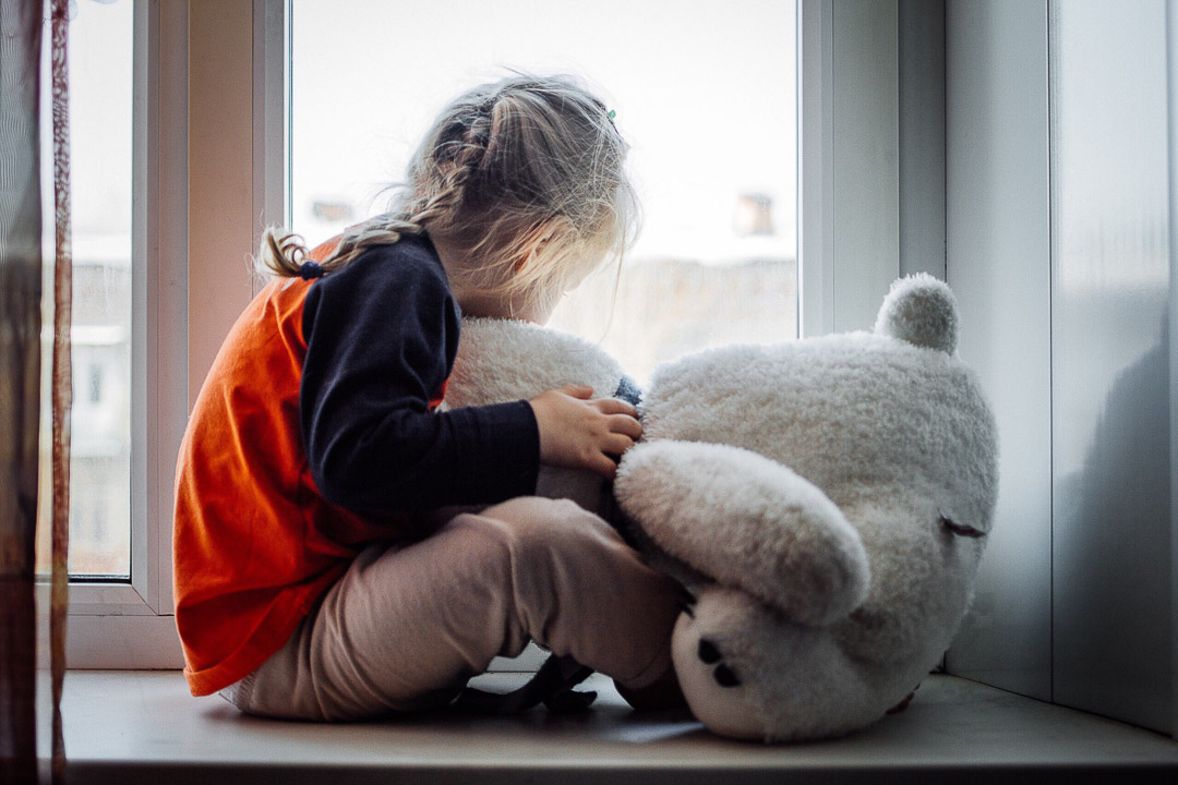 Sad child on the windowsill with his stuffed animal