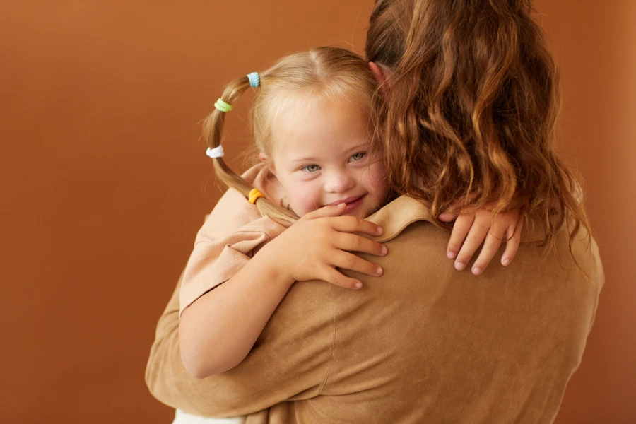Jeune enfant avec des besoins particuliers serrant un adulte dans ses bras, illustrant un moment de soutien et de réconfort.